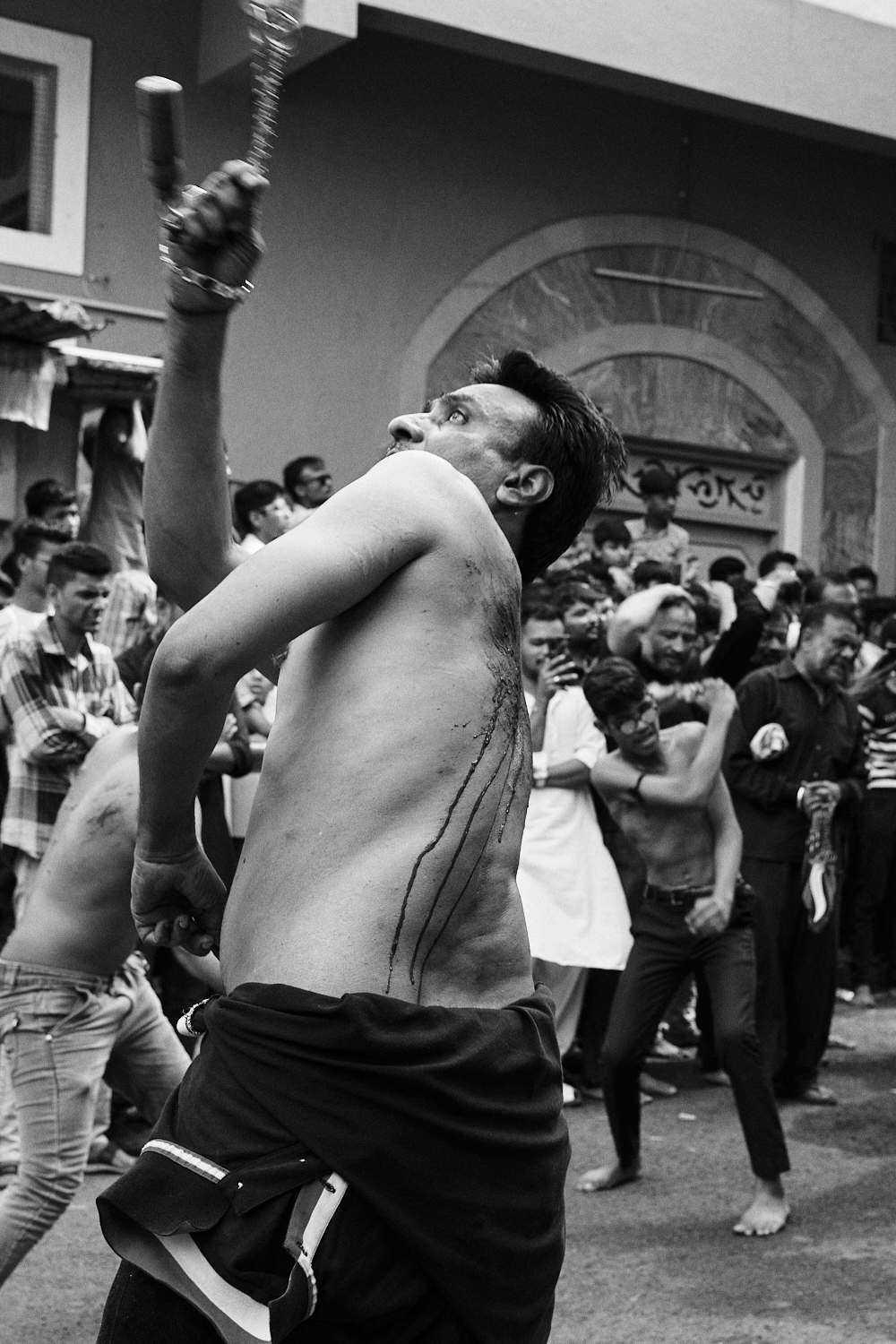 A man hits his bleeding back during Ashura/Muharram observance. Ahmedabad, India. 2023.