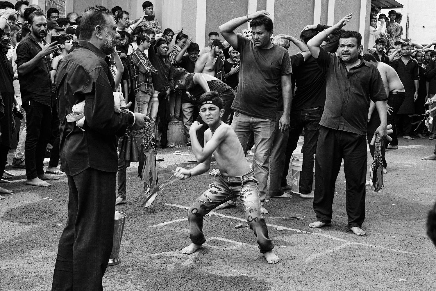 A young boy performs tatbir ritual by hitting himself on the back with a sharp object. Ahmedabad, India. 2023